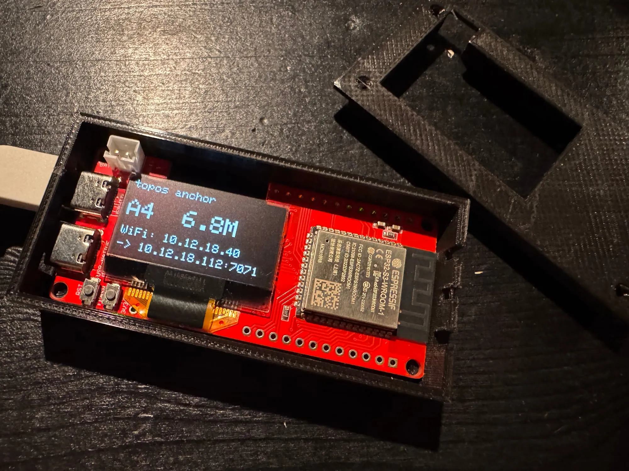 Ancre Topos ouverte : module MaUWB ESP32-S3 rouge dans la base du boîtier, couvercle clipsable posé à côté